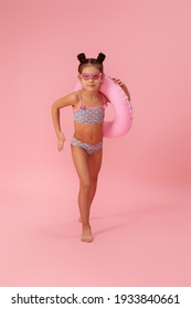 Little Child Girl In Swimwear With Inflatable Rubber Ring Running On Pink Background