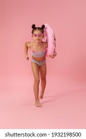 Little Child Girl In Swimwear With Rubber Ring Running On Pink Background