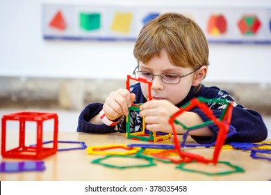 Little Child With Glasses Playing With Lots Of Colorful Plastic Blocks Kit In Maths Museum. Kid Boy Having Fun With Building And Creating Geometric Figures.