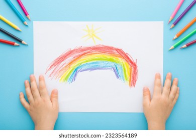 Little child hands showing colorful rainbow and sun shapes on white paper. Color pencils on light blue table background. Pastel color. Closeup. Point of view shot. Children creativity time. - Powered by Shutterstock