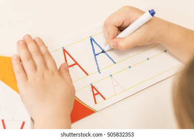 Little Child Hands Writing Letter A. Learning To Write. Little Girl Writing Alphabet In A Copy Book At A Desk. Learn Study Education School Knowledge Concept
