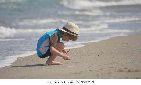 Little child with hat gathering shells on the beach, blue sea waving - Powered by Shutterstock