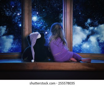 A Little Child And Her Teddy Bear Are Looking Outside A Window With Space Stars And Clouds In The Night For A Astronomy Or Dream Concept.