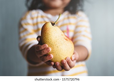 Little Child Holding A Pear Fruit In Her Hand With Selective And Shallow Depth Of Field Blurry Image. Concept Of Agriculture And Healthy Eating