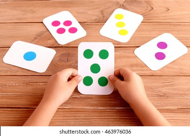 Little Child Holds A Training Card In His Hands And Learning The Color, Shape, Quantity. Colorful Flash Cards For Fun Teaching Kids. Early Development Concept. Wooden Background 