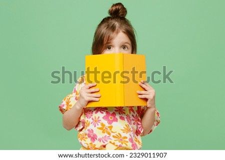 Little child kid girl 6-7 years old wear casual clothes have fun hold read cover mouth with book isolated on plain pastel green background studio portrait. Mother's Day love family lifestyle concept