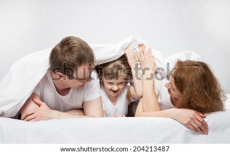 Little child lying in the bed between her parents, neutral background