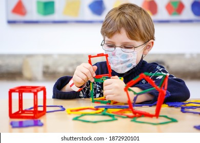 Little Child With Medical Mask Playing With Lots Of Colorful Plastic Blocks Kit In Preschool Nursery Or Elementary School. Cute Child Use Protective Equipment As Fight Against Covid 19 Corona Virus.