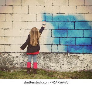 A little child is painting an old white brick wall with blue paint for creative art concept or design idea.
