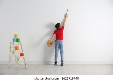 Little Child Painting On Blank White Wall Indoors