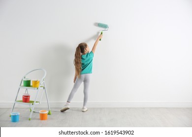 Little Child Painting With Roller Brush On White Wall Indoors