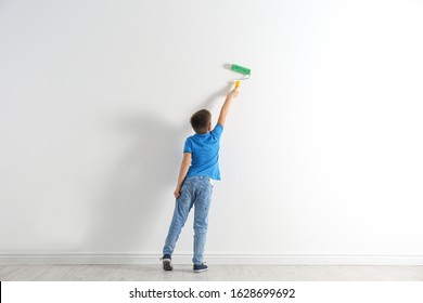 Little Child Painting With Roller Brush On White Wall Indoors