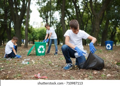 A little child picking up the garbage and putting it in a black garbage bag on a natural background. Ecology protection concept.