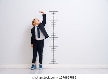 Little child is playing businessman. Kid is measuring the growth on the background of wall. Smart power concept. 