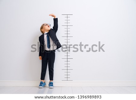 Little child is playing businessman. Kid is measuring the growth on the background of wall. Smart power concept. 