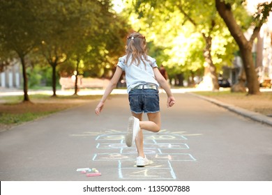 Little Child Playing Hopscotch Drawn With Colorful Chalk On Asphalt