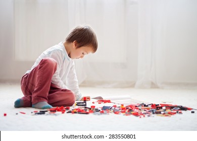 Little Child Playing With Lots Of Colorful Plastic Blocks Indoor, Building A Fire Truck And A Fire House, Reading From A Manual And Imagining