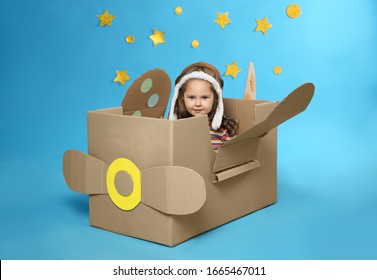 Little child playing with plane made of cardboard box near stars on blue background