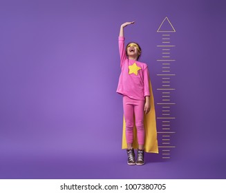Little child is playing superhero. Kid is measuring the growth on the background of bright ultraviolet wall. Girl power concept. Yellow, pink and  purple colors.