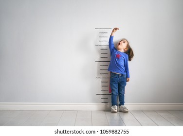 Little child is playing superhero. Kid is measuring the growth on the background of wall. Girl power concept.  - Shutterstock ID 1059882755