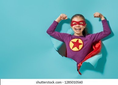 Little child is playing superhero. Kid on the background of bright blue wall. Girl power concept. 