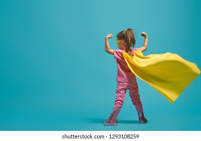 Little child playing superhero. Kid on the background of bright blue wall. Girl power concept. Yellow, pink and  turquoise colors.