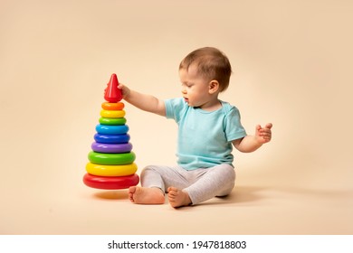 Little Child Plays An Educational Game. Baby Examines A Toy Pyramid. In The Studio On A Solid Background