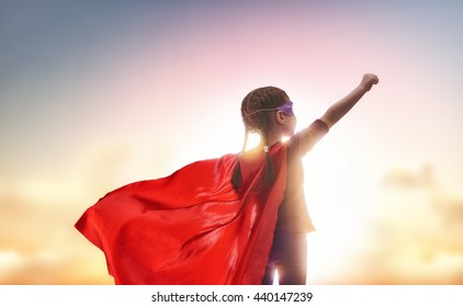 Little child plays superhero. Kid on the background of sunset sky. Girl power concept