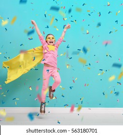 Little Child Plays Superhero. Kid On The Background Of Bright Blue Wall. Girl Is Throwing Confetti And Jumping. Yellow, Pink And  Turquoise Colors.