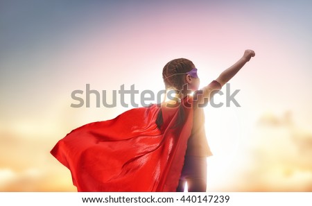 Little child plays superhero. Kid on the background of sunset sky. Girl power concept