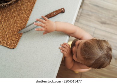 Little child reaching for knife on light countertop, above view. Dangers in kitchen - Shutterstock ID 2204513477