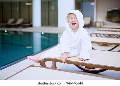 Little child relaxing after swimming in the pool, sitting on bed in white bathrobe. Cute kid enjoying active holidays in the resort. 
