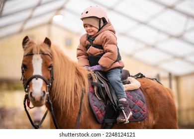 Little Child Riding Lesson. Three-year-old girl rides a pony and does exercises. High quality photo - Shutterstock ID 2248124121