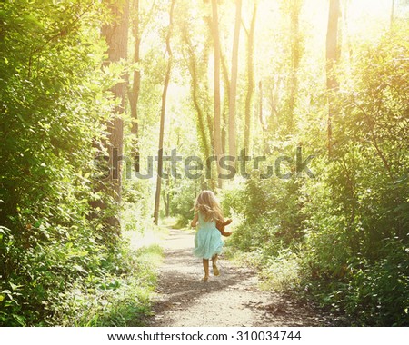 A little child is running down a nature trail with sunlight on the trees for a happiness or freedom concept.