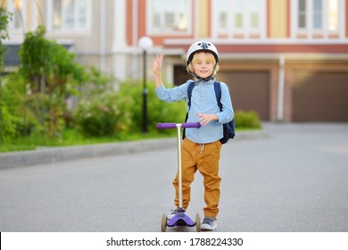 Little child in safety helmet riding scooter to school. Preschooler boy waving hand saying hi. Safety kids by way to school.