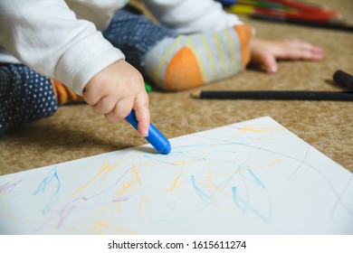 Little child is sitting on the floor and drawing lines with crayon on the white paper - Shutterstock ID 1615611274