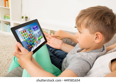 Little Child Sitting On Sofa Playing Game On Digital Tablet