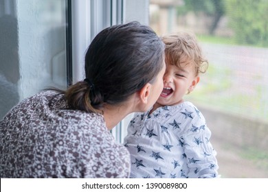 Little Child Sitting On Window Laughing With Mom. Mother And Child Eskimo Kisses.