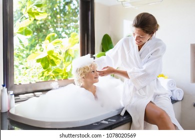 Little Child Taking Bubble Bath In Beautiful Bathroom With Big Garden View Window. Mother Washing Baby. Kids Hygiene. Shampoo, Hair Treatment And Soap Foam For Children. Mom Bathing Kid In Large Tub. 