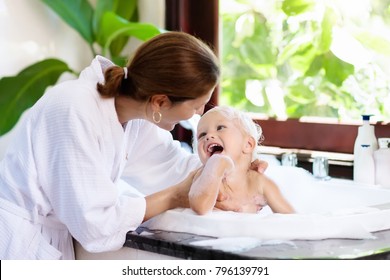 Little Child Taking Bubble Bath In Beautiful Bathroom With Big Garden View Window. Mother Washing Baby. Kids Hygiene. Shampoo, Hair Treatment And Soap Foam For Children. Mom Bathing Kid In Large Tub. 