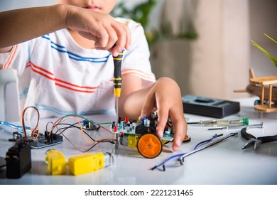 Little Child Tighten The Nut With A Screwdriver To Assemble Car Toy, Asian Kid Boy Assembling The Arduino Robot Car Homework Project At Home, Education AI Technology Workshop School Learning Lesson