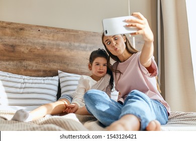 Little Child Together With Charming Mom Lying On Big Bed, Taking Selfie, Looking Away With Positive Expression, Having Fun In Morning Time, Shot From Below, Family Portrait