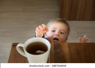 Little Child Try To Grab Cup Of Hot Tea On The Table. Attention Hot Content Concept.