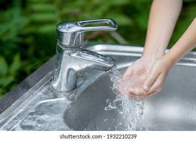 Little child washing hands with clean running water in the park. Coronavirus prevention hand hygiene. Concept hygiene, clean and health care. Flowing water from tap. Outdoor. Natural green background