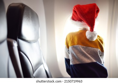 Little child wearing Santa Claus hat is traveling by an airplane. Preschooler boy is looking at aircraft window during flight. Family trip for winter holidays. Happy kid is waiting for merry Christmas - Powered by Shutterstock