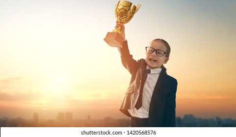 Little Child Is Winner. Kid On Sunset Background. Smart Power Concept. The Cup For First Place.