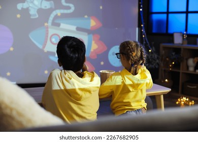 Little children in 3D glasses with popcorn watching cartoons on projector screen at home