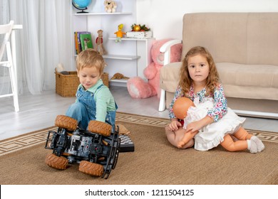 Little children, a boy and a girl, sit on the floor on a rug in the room at home and play with a toy car and a doll
