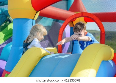 Little children climbing and leaping on red, blue and yellow giant inflatable bouncy slide outdoors during sunny day - Powered by Shutterstock