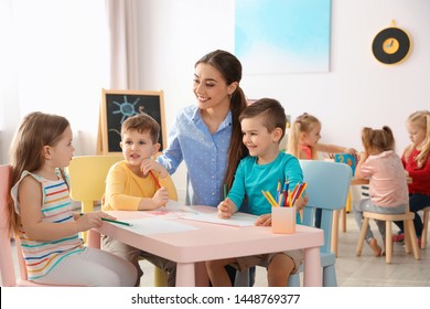 Kleine Kinder mit Kindergartenlehrer zeichnen an Tischen drinnen. Lernen und Spielen